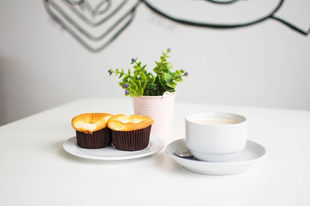 postre y café en el café con la planta plástica en el florero en la tabla blanca.