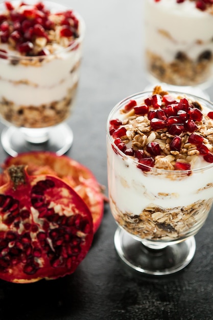 Postre casero fresco y saludable con muesli y granada sobre fondo de madera oscura