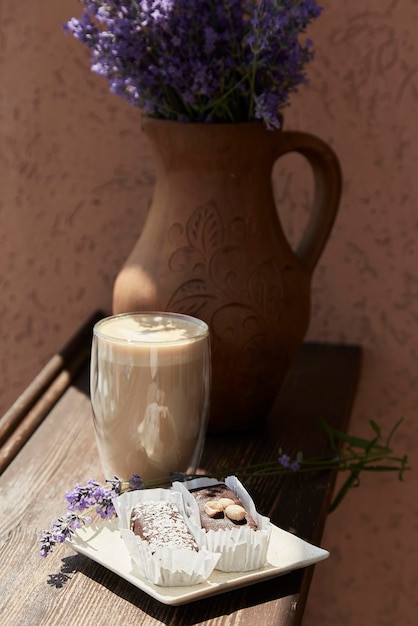 Postre de chocolate con un vaso de café con leche y flores de lavanda afuera en la terraza del café Desayuno de verano hora del café Sombras duras