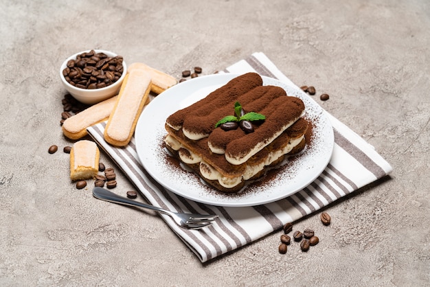 Postre clásico tiramisú y galletas savoiardi en placa de cerámica sobre mesa de hormigón