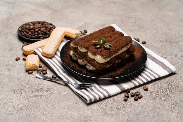 Postre clásico tiramisú y galletas savoiardi en placa de cerámica sobre mesa de hormigón