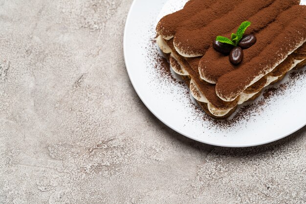 Postre clásico de tiramisú en plato de cerámica sobre superficie de hormigón gris claro