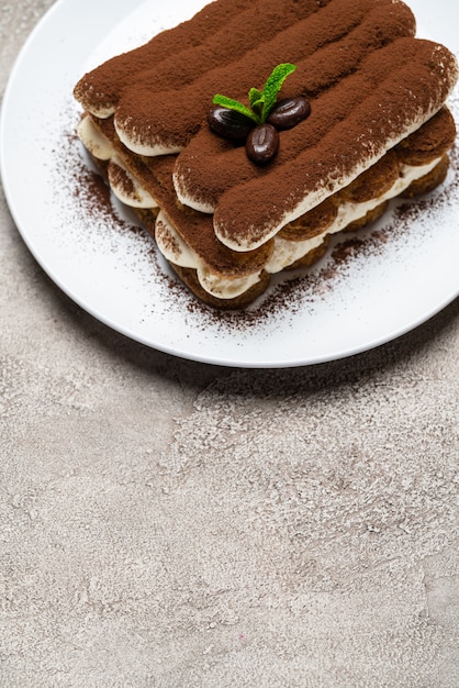 Postre clásico de tiramisú en plato de cerámica sobre superficie de hormigón gris claro