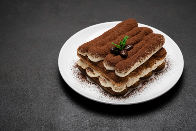 Postre clásico de tiramisú en plato de cerámica sobre superficie de hormigón oscuro