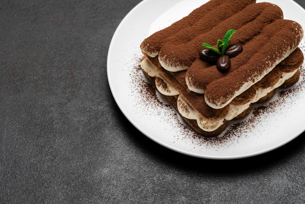 Foto postre clásico de tiramisú en plato de cerámica sobre superficie de hormigón oscuro