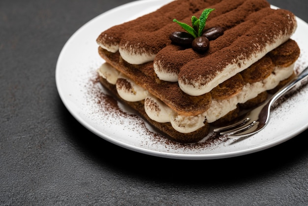 Postre clásico de tiramisú en plato de cerámica sobre superficie de hormigón oscuro