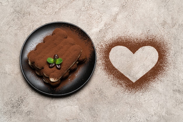 Postre clásico tiramisú sobre plato de cerámica y cacao en forma de corazón