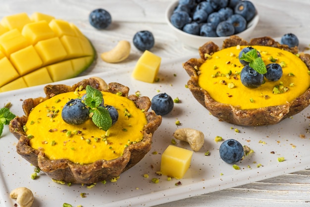 Postre de comida vegana. tortas veganas crudas de mango amarillo con arándanos frescos y menta. comida saludable sin gluten deliciosa