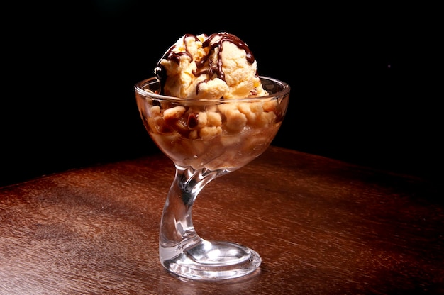 Postre de copa de helado con tarta de manzana y salsa de chocolate en tablexA de madera