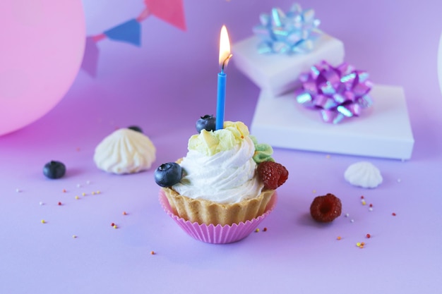 Postre con crema blanca decorada con bayas frescas y velas encendidas, fondo lila