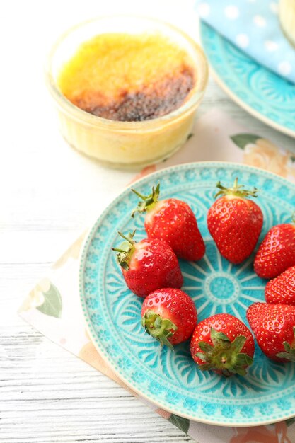 Postre creme brulee con bayas de fresa frescas en una servilleta sobre fondo de madera de color