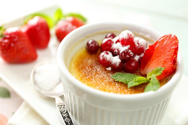 Postre creme brulee con fresas frescas y hojas de menta sobre fondo de madera de color