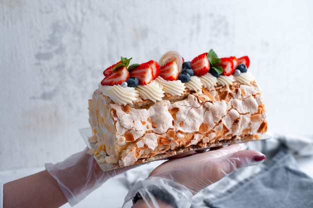 Postre delicado rollo de merengue con fresas y pétalos de almendra en manos de un pastelero