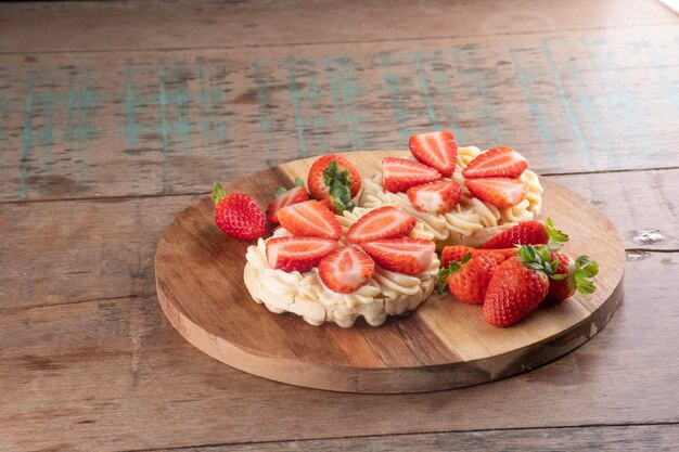 Postre de dos gofres con crema de chocolate blanco y trozos de fresa en una tabla redonda de madera y fresas cortadas en un paisaje de mesa de madera