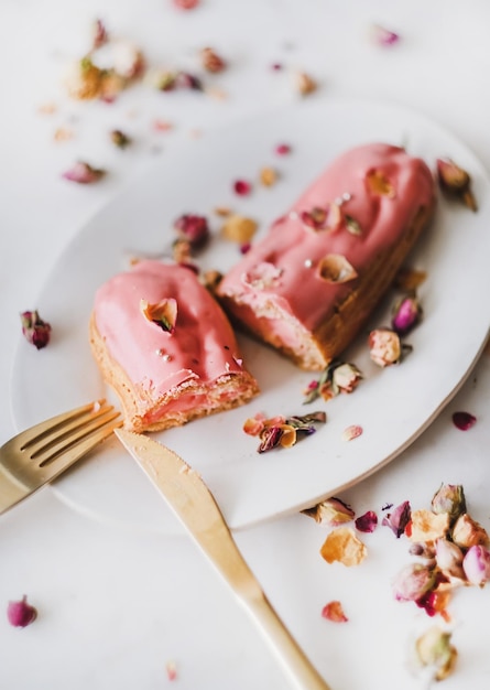 Postre eclair de rosa con pétalos de rosa secos en un plato blanco