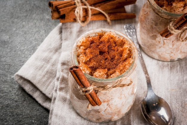 Postre español, sudamericano y mexicano. Gachas dulces, arroz con leche. Arroz con leche. En frascos en porciones, decorados con canela y azúcar. Sobre una mesa de piedra oscura. Copia espacio