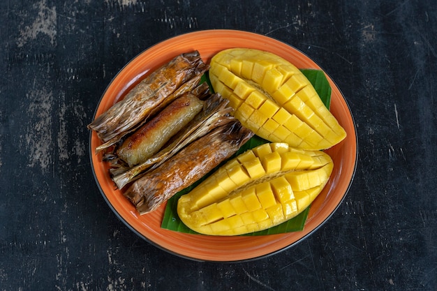 Postre estilo tailandés, mango amarillo con arroz glutinoso de plátano en hojas de palma. El mango amarillo y el arroz pegajoso es comida tradicional popular de Tailandia. De cerca