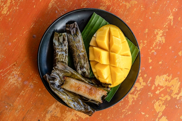 Postre estilo tailandés, mango amarillo con arroz glutinoso de plátano en hojas de palma. El mango amarillo y el arroz pegajoso es un postre tradicional popular de Tailandia. De cerca