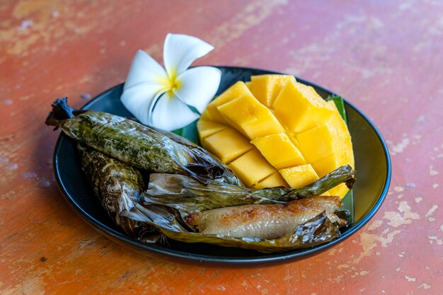 Postre estilo tailandés, mango amarillo con arroz glutinoso de plátano en hojas de palma. El mango amarillo y el arroz pegajoso es un postre tradicional popular de Tailandia. De cerca