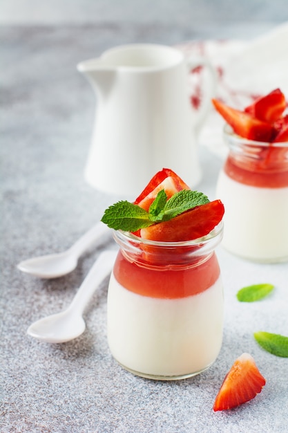 Foto postre festivo con gelatina de bayas, panna cota de vainilla y fresa fresca sobre fondo de mesa de hormigón gris. enfoque selectivo.