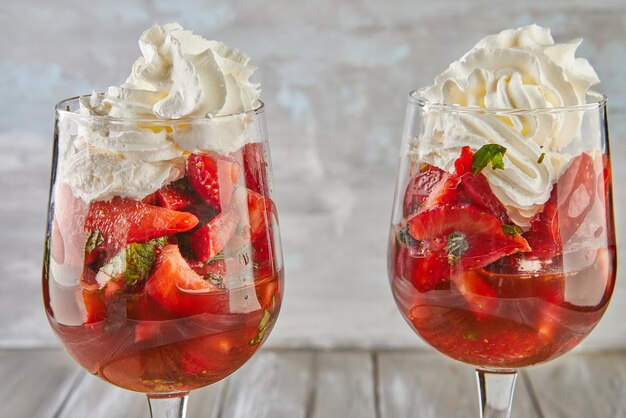 Postre de fresas y crema batida en vasos altos sobre fondo de madera