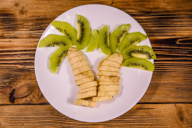 Foto postre de frutas saludables para niños con kiwi y plátanos en forma de palmera en un plato blanco vista superior
