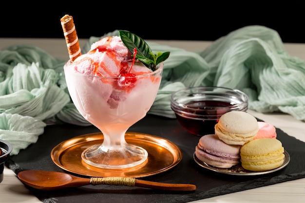 Un postre con helado de fresa en un vaso con una cuchara al lado.