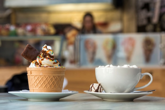 Postre helado en taza de oblea con galletas de chocolate y una taza de café con malvaviscos en plato de porcelana en el fondo del espacio colorido copia borrosa.