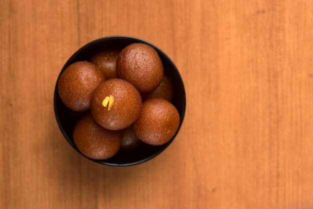 Postre indio o plato dulce: Gulab Jamun en un tazón sobre fondo de madera.