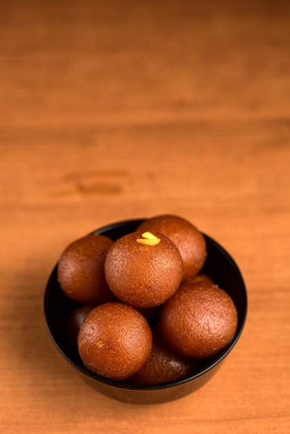 Postre indio o plato dulce: Gulab Jamun en un tazón sobre fondo de madera.