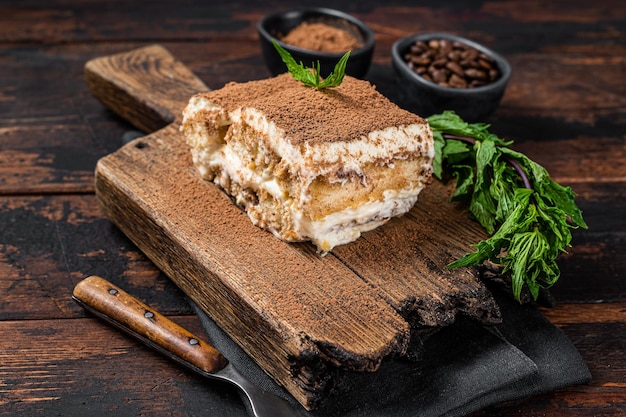 Postre italiano Pastel de tiramisú con cacao y menta sobre una tabla de madera. Fondo de madera oscura. Vista superior.