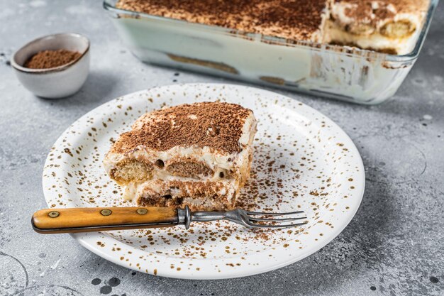 Postre italiano de tiramisú cubierto con cacao en un plato. Fondo gris. Vista superior.