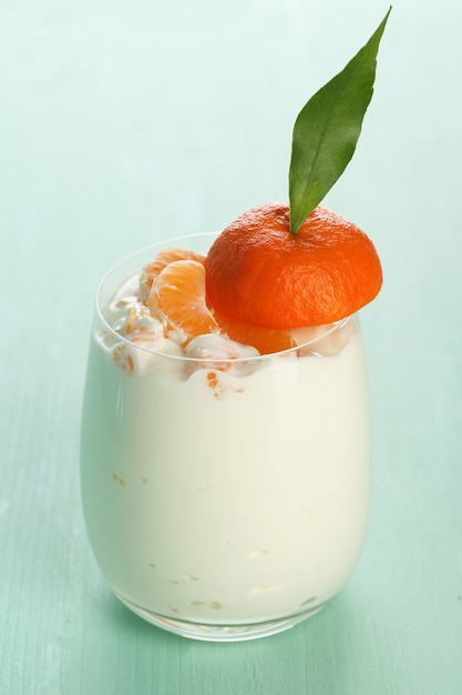 Postre de leche sabroso con trozos de mandarina fresca en vidrio, sobre mesa de madera de color