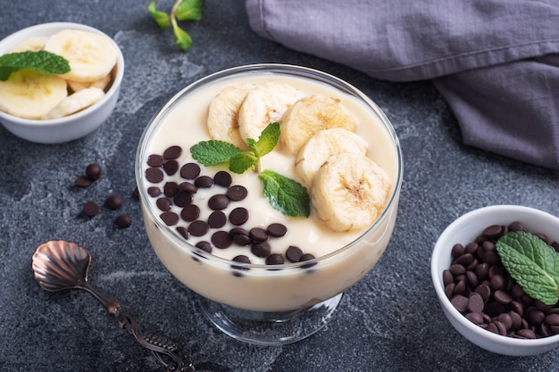 Postre con leche, yogur, plátano y chocolate en un vaso sobre fondo azul oscuro