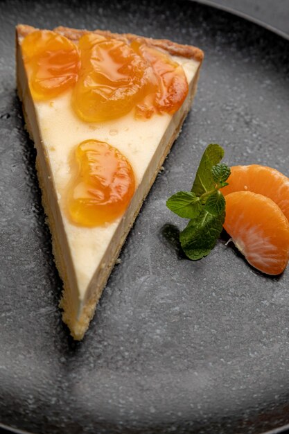 Postre de mandarina adornado con gajos de mandarina y menta, servido en un plato negro. plato sobre fondo negro de navidad