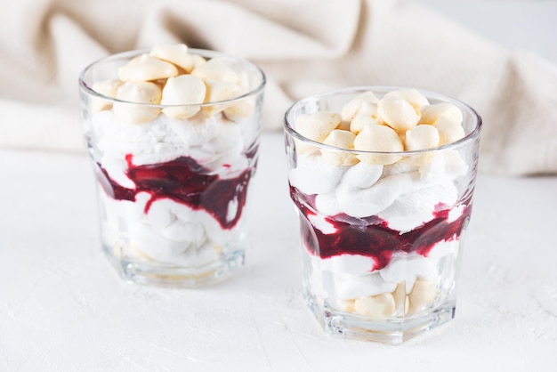 Postre con merengue de aquafaba, crema de coco y cerezas en vasos sobre una mesa de luz.