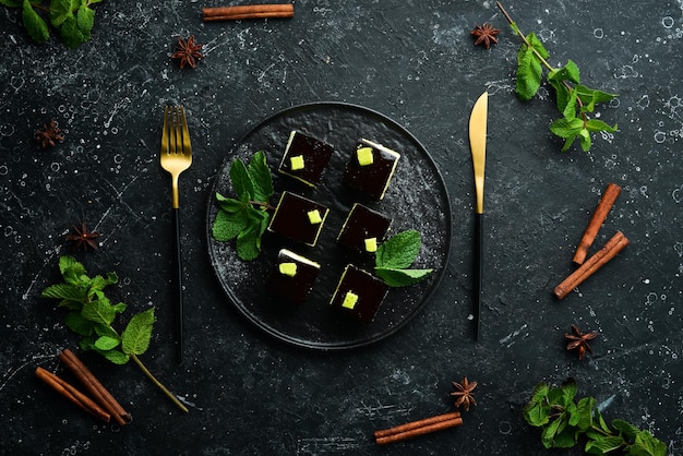 Postre de mousse de chocolate Ópera en un plato negro con menta Vista superior Estilo rústico