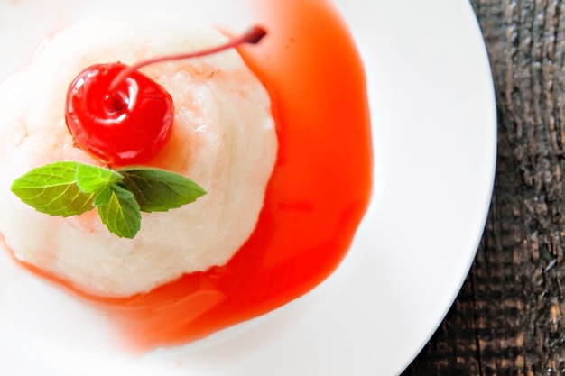 Foto postre de mousse de crema aireado blanco con jarabe de menta cereza sobre fondo de madera oscura