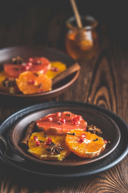 Postre de naranja con miel de vino o jarabe de arce y bayas de granada decoradas con especias de jengibre Comida maravillosamente dulce, rica y fresca Espacio de copia de fondo rústico oscuro para su texto