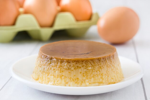 Postre de las natillas del caramelo en el plato blanco con la superficie de madera.