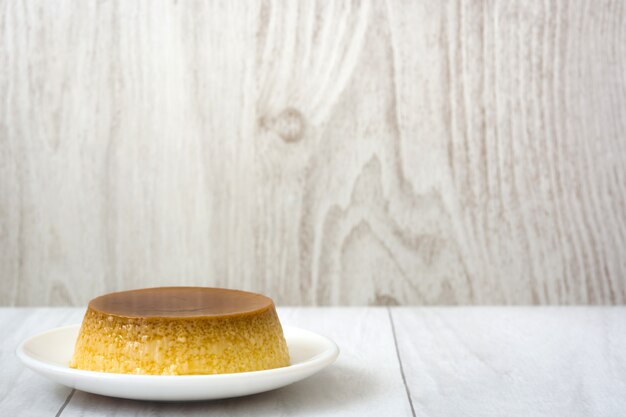 Foto postre de las natillas del caramelo en el plato blanco con la superficie de madera.