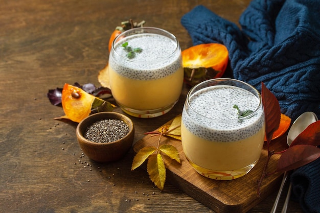 Postre de otoño Panna cotta casera con fruta de caqui y semillas de chía en una mesa de madera Espacio de copia