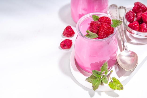 Postre de panna cotta de frambuesa con frambuesas frescas y hojas de menta melissa Panna cotta rosa en frascos de porción pequeña sobre un fondo blanco