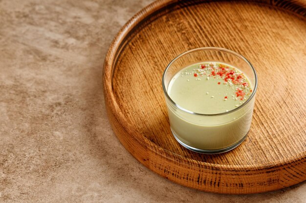 Foto un postre de panna cotta de té matcha con decoración en un vaso sobre una bandeja de madera y fondo beige