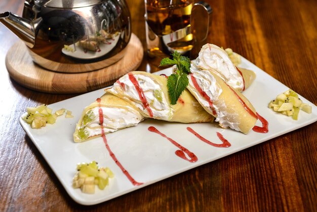 Postre Panqueques con crema y fruta Decorado con jarabe y menta sobre una mesa de madera