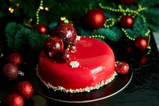 Postre de pastel de pastelería de Navidad de mousse cubierto con esmalte de espejo rojo con adornos de año nuevo en luces de guirnalda bokeh fondo oscuro, tema de Navidad de pastel europeo moderno.