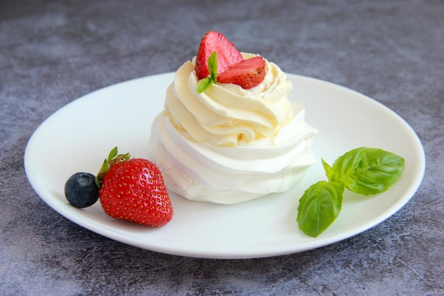 Postre Pavlova casero: merengue con crema batida, menta y bayas frescas en el plato