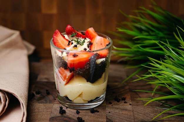 Un postre rico con fresas y galletas de chocolate en un vaso sobre una base de madera