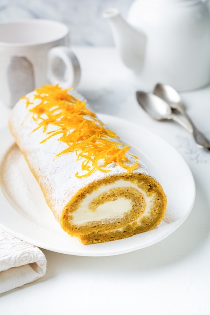 Postre rollo de calabaza con crema de mantequilla y servidor de naranja para la mesa festiva en mesa gris claro. Enfoque selectivo.