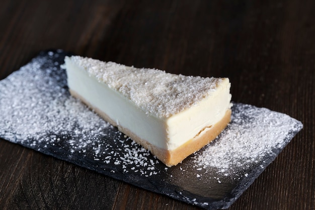 Postre de tarta de queso cubierta con pulpa de coco seca, tarta de queso en bandeja individual espolvoreada con azúcar en polvo